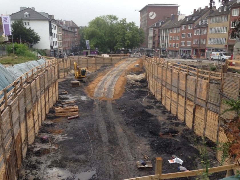 Eine ziemlich große Baugrube. Im Hintergrund, rechts, das Gebäude der Handwerkskammer.